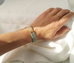 a woman's hand on top of a white sheet wearing a gold and green bracelet