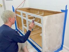 a man kneeling on the ground working on some cabinet doors with wires attached to them