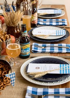 the table is set with blue and white place mats, silverware, beer, and pretzels