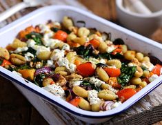 a casserole dish filled with pasta, vegetables and cheese on a wooden table