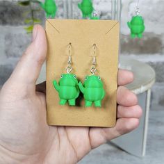 a pair of green frog earrings sitting on top of a piece of cardboard next to a table