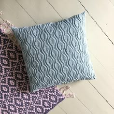 two blue and pink pillows sitting on top of a white wooden floor next to each other