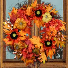 a wreath with orange and yellow leaves on it in front of a wooden window frame