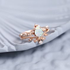 an opal and diamond ring sits on top of a white satin material with gold accents