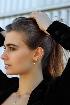 a woman with her hair in a ponytail and wearing gold earrings, looking off to the side