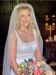 a woman in a wedding dress holding a bouquet of flowers and smiling at the camera