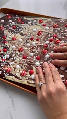 two hands are decorating a chocolate cake with red and white decorations on it's surface