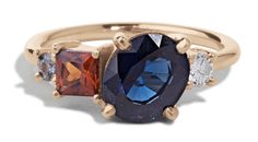 three stone ring in yellow gold with two different colored stones on the band and one blue,