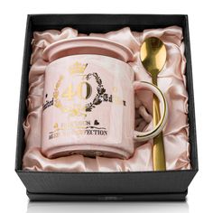 a pink coffee mug in a gift box with a gold spoon and fork next to it