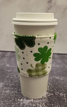 a coffee cup sleeve with shamrocks and polka dots on white fabric, sitting on a table