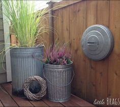 two metal buckets sitting on top of a wooden deck next to a potted plant