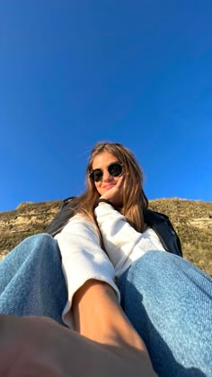 a woman sitting on the ground with her feet up in the air and wearing sunglasses