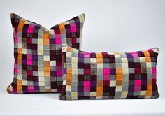 two colorful pillows sitting next to each other on a white surface with no one in the photo