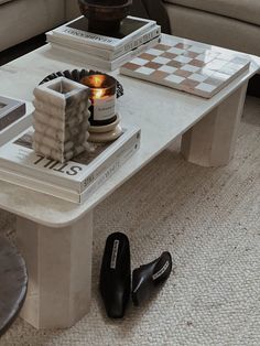 a white coffee table with candles and books on it next to black shoes in front of a couch