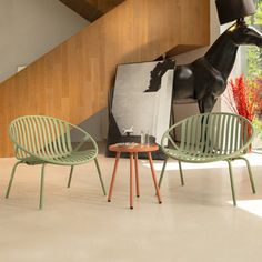 two green chairs sitting next to each other in front of a horse statue on the wall