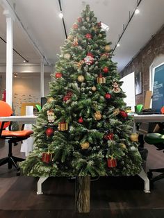 a decorated christmas tree in an office cubicle with orange chairs and desks behind it