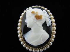 "Pre-Owned For Sale: (1) Beautiful Antique Carved Dark Shell Cameo Brooch in 14k Yellow Gold PLEASE READ ENTIRE DESCRIPTION BEFORE PURCHASING This beautiful carved cameo brooch is in good condition for its age. The brooch features a lovely lady in white with curls wearing flowers in her hair from the dark shell background. This piece is not marked but has been tested to 14k yellow gold. The cameo has a gold frame surrounded by pearls. We believe this piece to be from the Victorian Ear around the Elegant Cameo Brooch For Formal Wear, Elegant Formal Cameo Brooch, Elegant Formal Brooch With Intaglio Detail, Luxury Intaglio Brooch For Formal Occasions, Elegant Intaglio Brooch For Formal Occasions, Elegant Oval Intaglio Brooches, White Cameo Brooch For Formal Occasions, White Cameo Brooches For Formal Occasion, Exquisite White Brooch For Formal Occasions