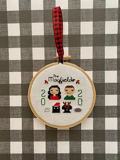 a cross stitch ornament hanging from a red ribbon on a black and white checkered tablecloth