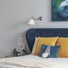 a bed with yellow and blue pillows in a bedroom next to a painting on the wall