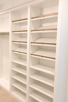 an empty walk in closet with white shelving and wooden shelves on the wall,