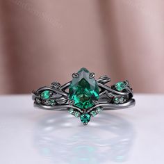 a ring with an emerald colored stone surrounded by green diamonds on a white table top