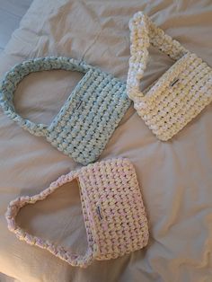 three crocheted purses sitting on top of a white bed next to each other