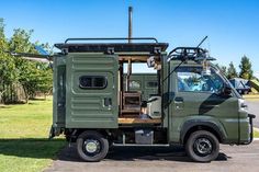 an army green truck parked on the side of a road next to a tree filled field