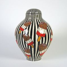 a black and white striped vase with red designs on the top, sitting in front of a white background