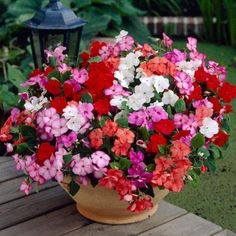 colorful flowers in a pot sitting on a wooden table next to a lamp post and green grass