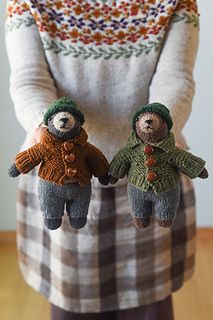 two stuffed bears are held in the hands of a woman wearing a sweater and hat