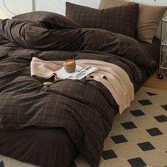 an unmade bed with brown comforter and coffee cup on the floor next to it