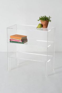 a stack of books sitting on top of a clear shelf next to a potted plant