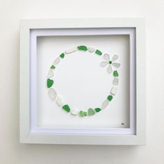 a white frame holding a green and white beaded necklace in it's shadow