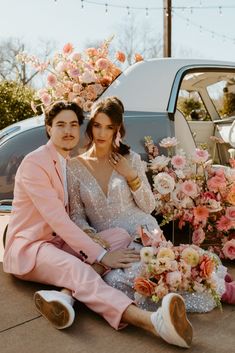 a man and woman sitting on the ground next to a car with flowers in it