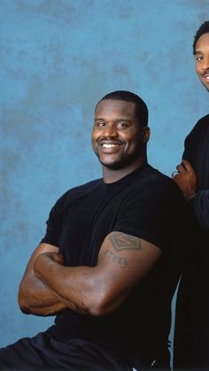 two men standing next to each other in front of a blue background with one smiling at the camera