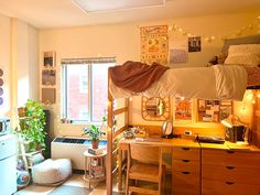 a dorm room with bunk beds, desk and window in the corner is lit by string lights