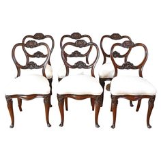 four chairs with white upholstered seats and wood trimming on the back side