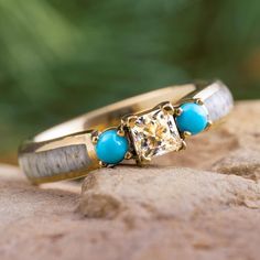 two yellow gold rings with turquoise stones on top of each other sitting on a rock