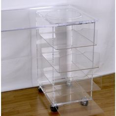 a clear acrylic cart with four drawers and wheels on the bottom, sitting on a hard wood floor