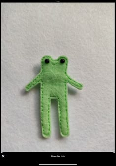 a green felt frog brooch with eyes on it's back, sitting on a white surface