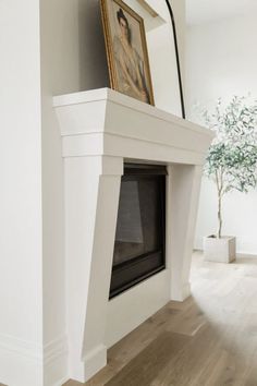 a white fireplace with a painting on the mantle next to it and a potted plant