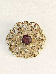 Gold Tone with Purple glass gem stone vintage brooch or scarf pin.  This is a very pretty pin in bright gold colour and has a leaf style scroll design in a round ish configuration.  It is 1 1/2" X 1 1/2" with a glass centre piece that is about 3/8" wide. It is in excellent condition with a secure C clasp.  It is nit marked by a maker. Please See the Pictures for condition, sized and identification confirmation. Let's try together to encourage Upcycling and Repurposing.  This is the perfect examp Victorian Gold Brooches With Intricate Design, Gold Victorian Brooches With Intricate Design, Victorian Gold Brooch With Intricate Design, Gold Victorian Brooch With Intricate Design, Elegant Round Brooch With Intricate Design, Elegant Round Brooches With Intricate Design, Victorian Gold Brooches For Formal Occasions, Gold Victorian Brooches For Formal Occasions, Heirloom Gold Brooch With Intricate Design