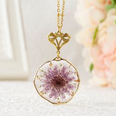 a necklace with a purple flower in it on a white table next to pink flowers