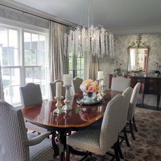 a dining room table with chairs and chandelier in front of large glass windows