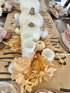 the table is set with white pumpkins, leaves and candles