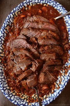 a blue and white bowl filled with meat covered in sauce on top of a wooden table