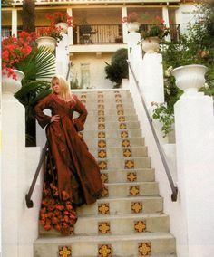 a woman in a long dress standing on the steps to a house with flowers painted on it