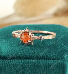 an orange diamond ring sitting on top of a green velvet box with a gold band