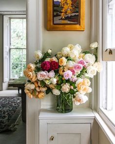 a vase filled with lots of flowers sitting on top of a white table next to a window