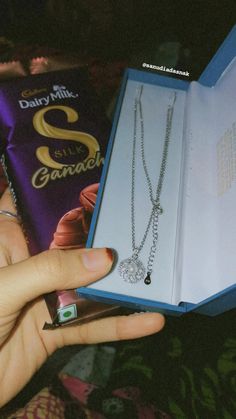 a person holding an open book with some jewelry in it's hand and a chocolate bar on the other side